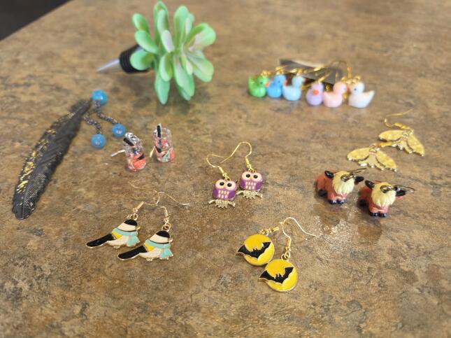 Whimsical earrings and a feather-shaped bookmark by Colorado Springs maker Stephanie Copus, featuring birds, owls, bats, moths, and other colorful designs.