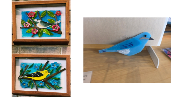 Framed fused-glass chickadee and American Goldfinch artwork with flowers alongside a bluebird suncatcher by Colorado Springs artist Jenny Paradis.