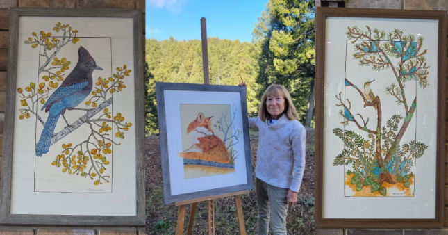 Artist Kathy Crowther standing beside an original framed fox painting, shown between her framed Steller&rsquo;s Jay and hummingbird nature paintings.