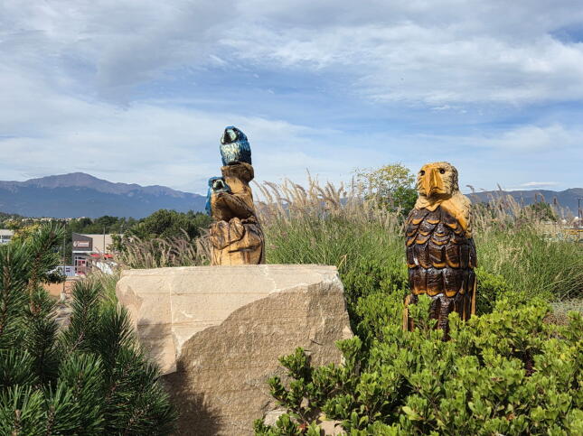 Hand-carved wooden eagle and two blue birds displayed in landscaping outside Wild Birds Unlimited of Colorado Springs, with Pikes Peak in the background.